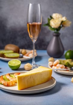 Wedge of gourmet cheese is served with shrimp, kiwi slices, and a glass of sparkling wine, creating an elegant and appetizing culinary scene