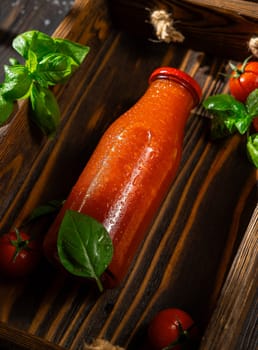Refreshing tomato juice with basil presented in a glass bottle on a rustic wooden tray, creating a vibrant and natural image