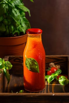Glass bottle of refreshing tomato juice decorated with basil leaf, placed on wooden tray, promoting healthy and natural beverage options