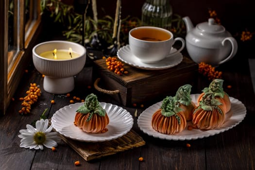 Delicious pumpkin shaped desserts served with tea, creating a warm and inviting autumn atmosphere by the candlelight