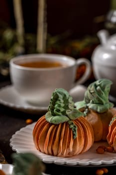 Pumpkin shaped desserts sitting on a white plate with a cup of tea and a teapot in the background, creating a cozy autumn scene