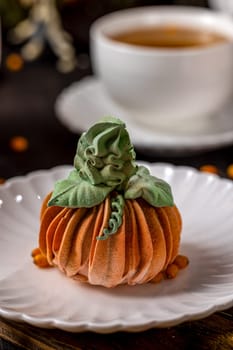 Pumpkin-shaped dessert sits on a white plate, evoking autumnal flavors and treats, with a cup of tea completing the cozy scene