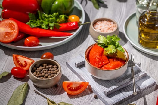 Small bowl of pickled red pepers, accompanied by fresh vegetables, spices, and olive oil, showcasing a colorful and appetizing culinary arrangement