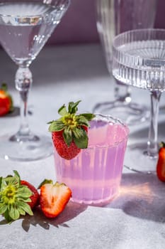 Vibrant pink strawberry cocktail, garnished with fresh strawberries, served in a stylish glass alongside elegant glassware