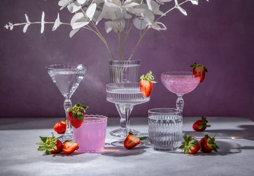 Pink cocktail, water, and fresh strawberries served in elegant glassware, creating a stylish and refreshing scene