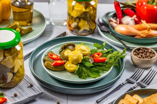 Pickled pattypan squash, gherkins, and chili peppers are served on a plate with fresh herbs, creating a vibrant and appetizing presentation