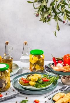 Pickled pattypan squash and gherkins on a plate, garnished with fresh herbs, alongside jars of pickles, oil, and spices