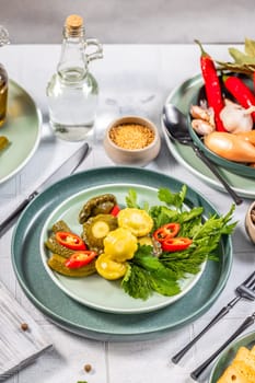 Pickled pattypan squash and cucumber salad arranged on a plate with fresh herbs, spices, and chili peppers, creating a vibrant and appetizing presentation