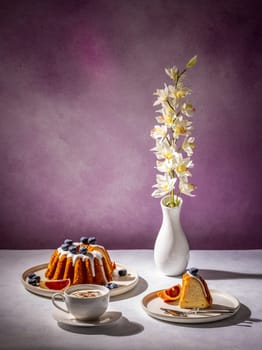 Gugelhupf cake with icing, blueberries, orange slices, cappuccino and orchid flower in a vase, creating a cozy and inviting atmosphere