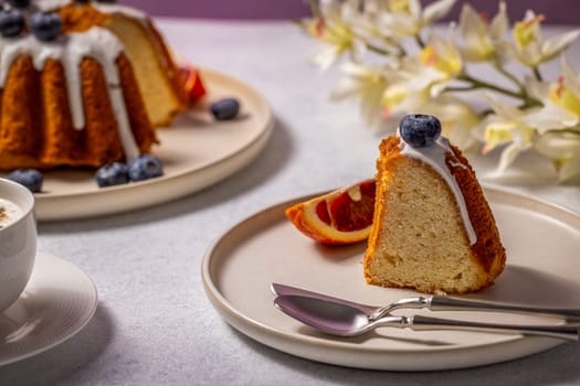 Slice of gugelhupf cake with icing, blueberries and a slice of blood orange, ready to be enjoyed with a cup of cappuccino