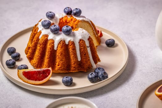 Sliced gugelhupf cake, decorated with icing, blueberries and blood orange, served on a plate