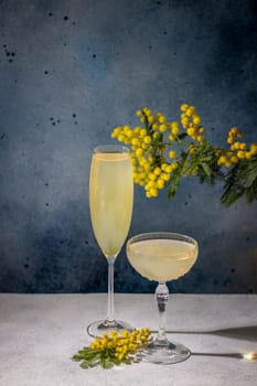 Two glasses of mimosa cocktail garnished with mimosa flowers, celebrating the arrival of spring with a refreshing drink