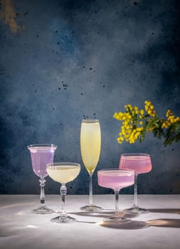 Four elegant glasses filled with vibrant cocktails, accompanied by a mimosa flower, create a celebratory atmosphere, perfect for special occasions