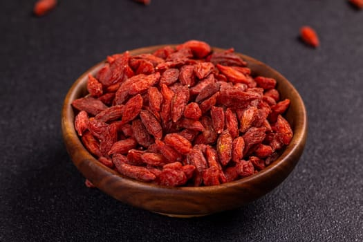 Close up of nutritious dried goji berries overflowing a wooden bowl, showcasing their vibrant red color and potential health benefits