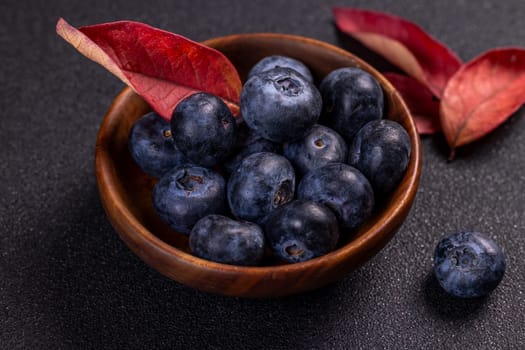 Ripe blueberries overflowing a small wooden bowl, accented by vibrant autumn leaves, create a tempting display on a dark, textured surface
