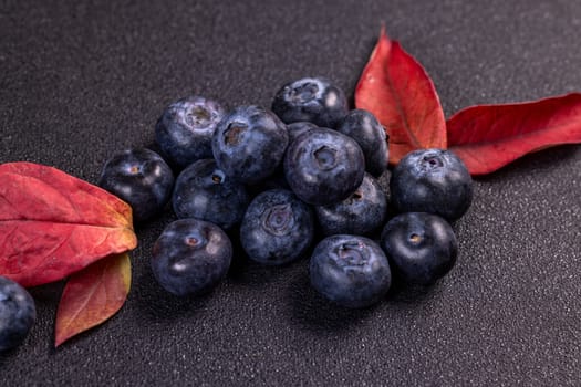 Ripe blueberries and colorful autumn leaves arranged on a dark background, offering a striking color contrast