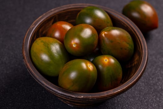 Fresh, ripe kumato tomatoes are displayed in a rustic bowl, showcasing their unique dark green and reddish brown hues against a dark background