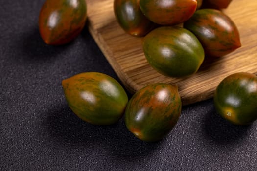 Ripe green kumato tomatoes are scattered on a dark textured surface and wooden cutting board, creating a visually appealing arrangement