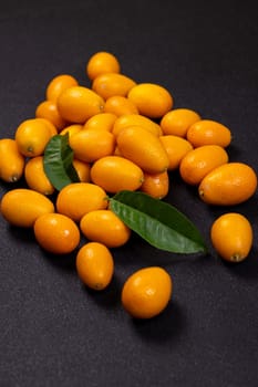 Fresh kumquat fruits nestled among vibrant green leaves create a striking display against a dark background, highlighting their juicy appeal