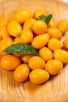 Fresh kumquats with leaves are creating a vibrant display on a wooden plate, showcasing the beauty of nature's bounty