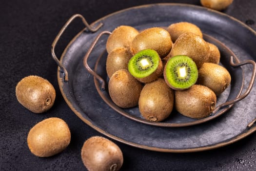 Ripe kiwi fruits are presented on a dark metal tray, showcasing their vibrant green flesh and fuzzy brown skin