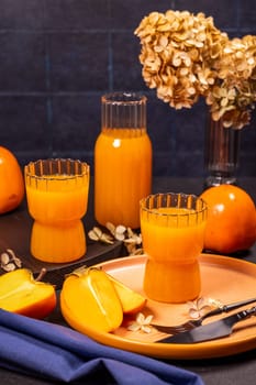 Arranging two glasses and a bottle of persimmon juice with fresh fruits, dried flowers, and cutlery creates a vibrant scene