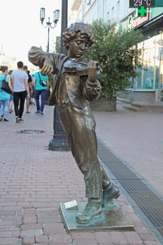 Nizhny Novgorod, Russia - August 27, 2016 - A bronze sculpture of a boy playing the violin captivates passersby on a busy street