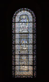 Intricate stained glass window illuminates the interior of Saint-Sernin basilica with vibrant biblical narratives.