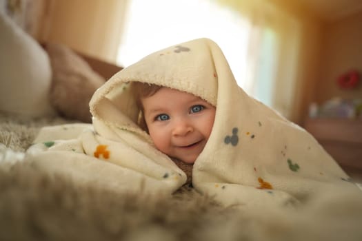 Smiling baby girl crawling on bed under the blanket. Adorable kid portrait. 6 month old child. Childhood concept. High quality photo