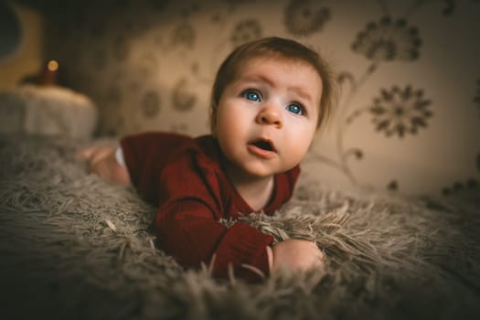 Blue-eyed baby girl in red clothes close up crawling on bed. Adorable kid portrait. 5 month old child. Childhood concept. High quality photo