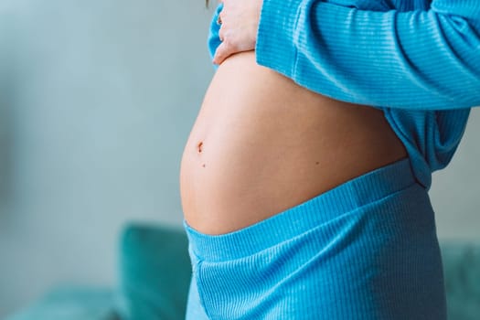 Close-up of young pregnant woman touching her belly on 6th month of pregnancy and caring about her health. Motherhood and baby expectation concept. High quality photo