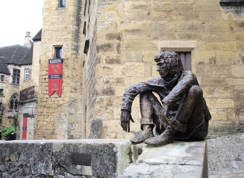 Sarlat-la-Caneda, France - October 10, 2016 - Bronze statue of Le Badaud, The Onlooker, a young man by a stone wall