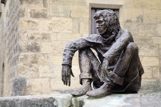 Sarlat-la-Caneda, France - October 10, 2016 - Bronze statue of Le Badaud, The Onlooker, a young man by a stone wall