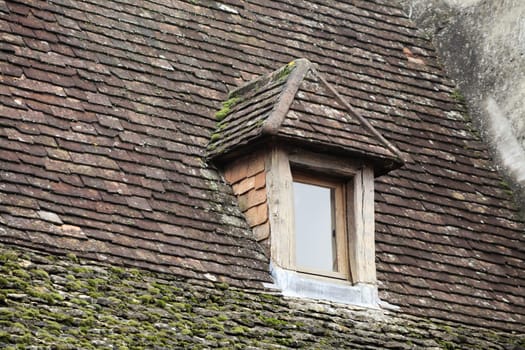 A charming wooden window on a mossy slate roof in Sarlat-la-Caneda showcases classic French rural design.