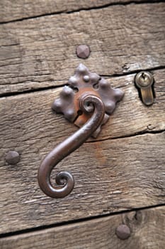 Close-up view of an ornate metal latch on a rustic wooden door in Sarlat-la-Caneda, highlighting local artisan skills.