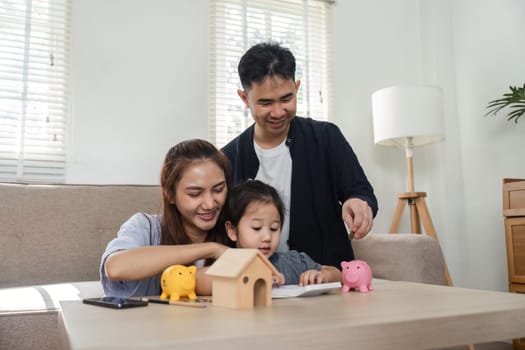 A family sits together, teaching their child about saving money using piggy banks and a notebook.