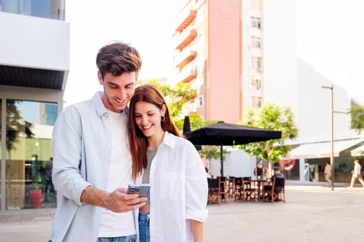 man and woman smiling happy looking a cell phone together, they are enjoying the moment and sharing something on the phone, concept of technology of communication and social media, copyspace for text