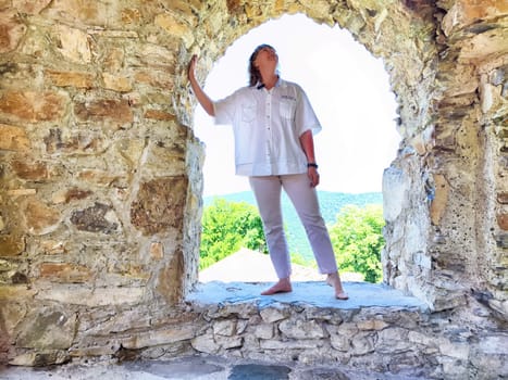 Individual poses confidently in a stone arch, enjoying the serene view of green hills in bright daylight.