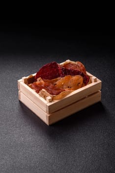 Jerky, dried meat in the form of slices with salt, spices and herbs on a dark concrete background