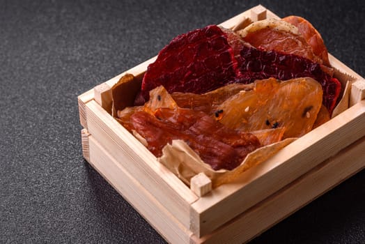 Jerky, dried meat in the form of slices with salt, spices and herbs on a dark concrete background