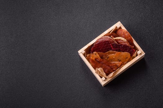 Jerky, dried meat in the form of slices with salt, spices and herbs on a dark concrete background
