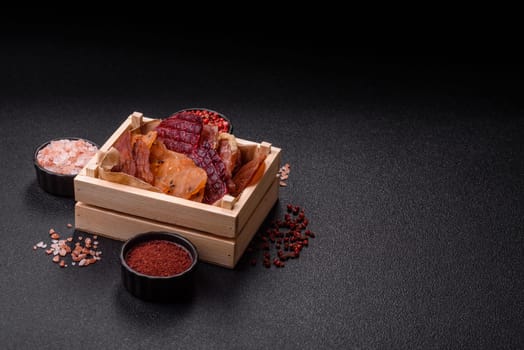 Jerky, dried meat in the form of slices with salt, spices and herbs on a dark concrete background