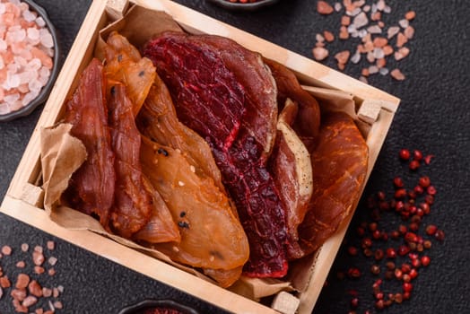 Jerky, dried meat in the form of slices with salt, spices and herbs on a dark concrete background