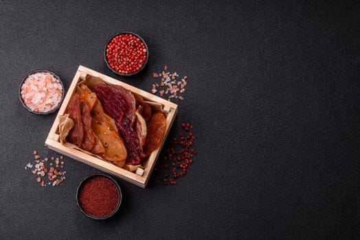 Jerky, dried meat in the form of slices with salt, spices and herbs on a dark concrete background