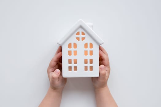 Child holding ceramic house model with warm glow in room.