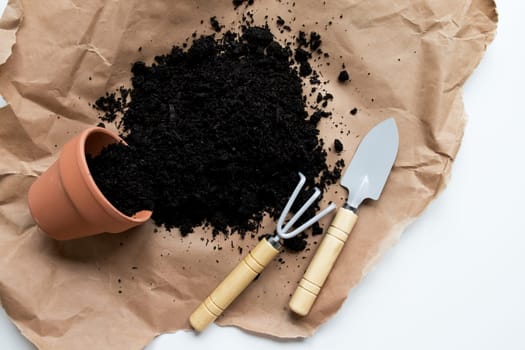 Garden tools with soil and pot on brown paper background.
