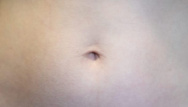 This close-up shows a human abdomen with focus on the navel and skin texture. The lighting highlights subtle details, emphasizing the natural form of the body.
