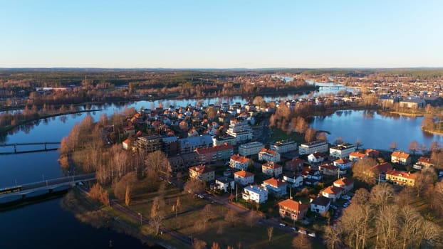 A beautiful aerial view of Karlstad, Sweden, showcasing winding rivers, bridges, and charming houses with red roofs, bathed in warm golden sunset light, creating a peaceful Scandinavian scene.