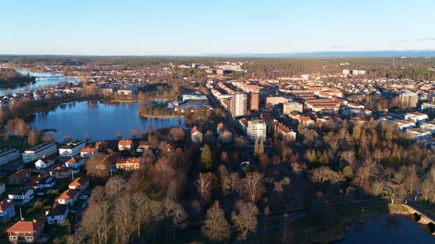 A scenic aerial view of Karlstad, Sweden, featuring lakes, lush parks, and residential areas bathed in golden sunset light, blending nature and urban charm in a peaceful Nordic setting.