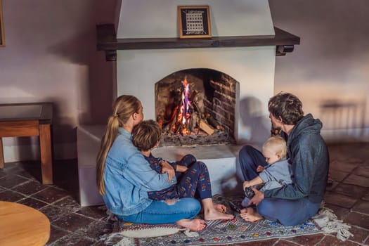 Family bonding by the fireplace during cozy winter evening. Warm and peaceful family moment indoors. Togetherness, love, and relaxation concept. A warm and inviting scene featuring a lit fireplace with glowing firewood and candles. A colorful traditional rug and pillow lie on the floor, creating a cozy atmosphere. Home, relaxation, and rustic comfort concept.